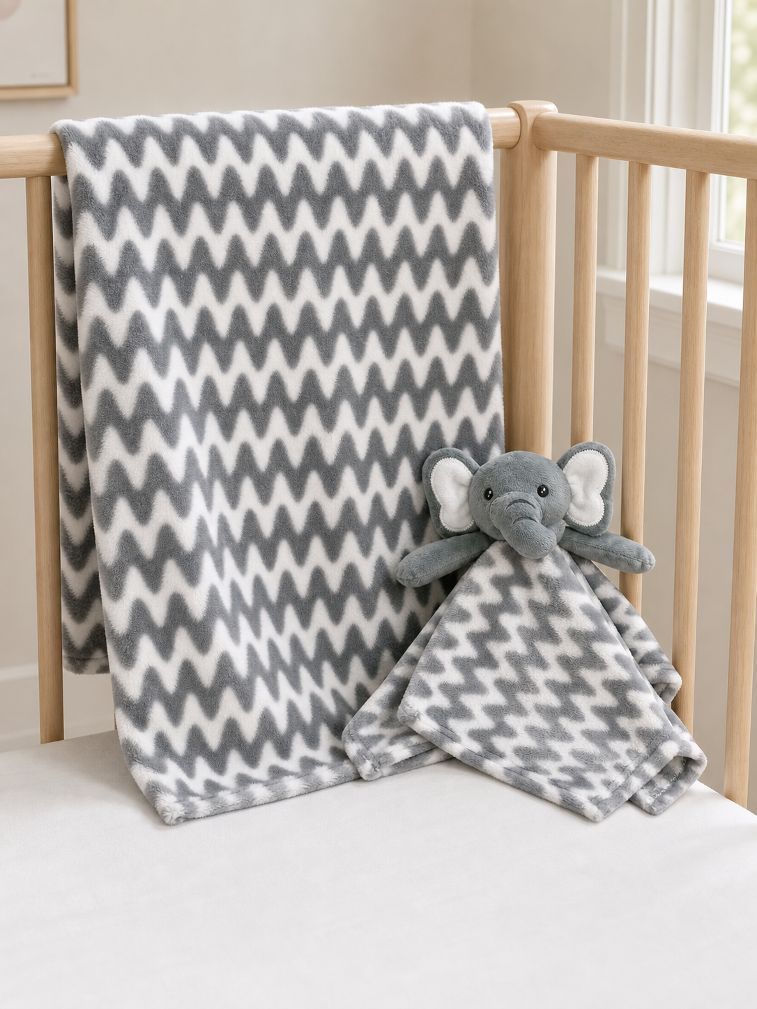 Grey elephant blanket and Nunu lovey set arranged in a crib