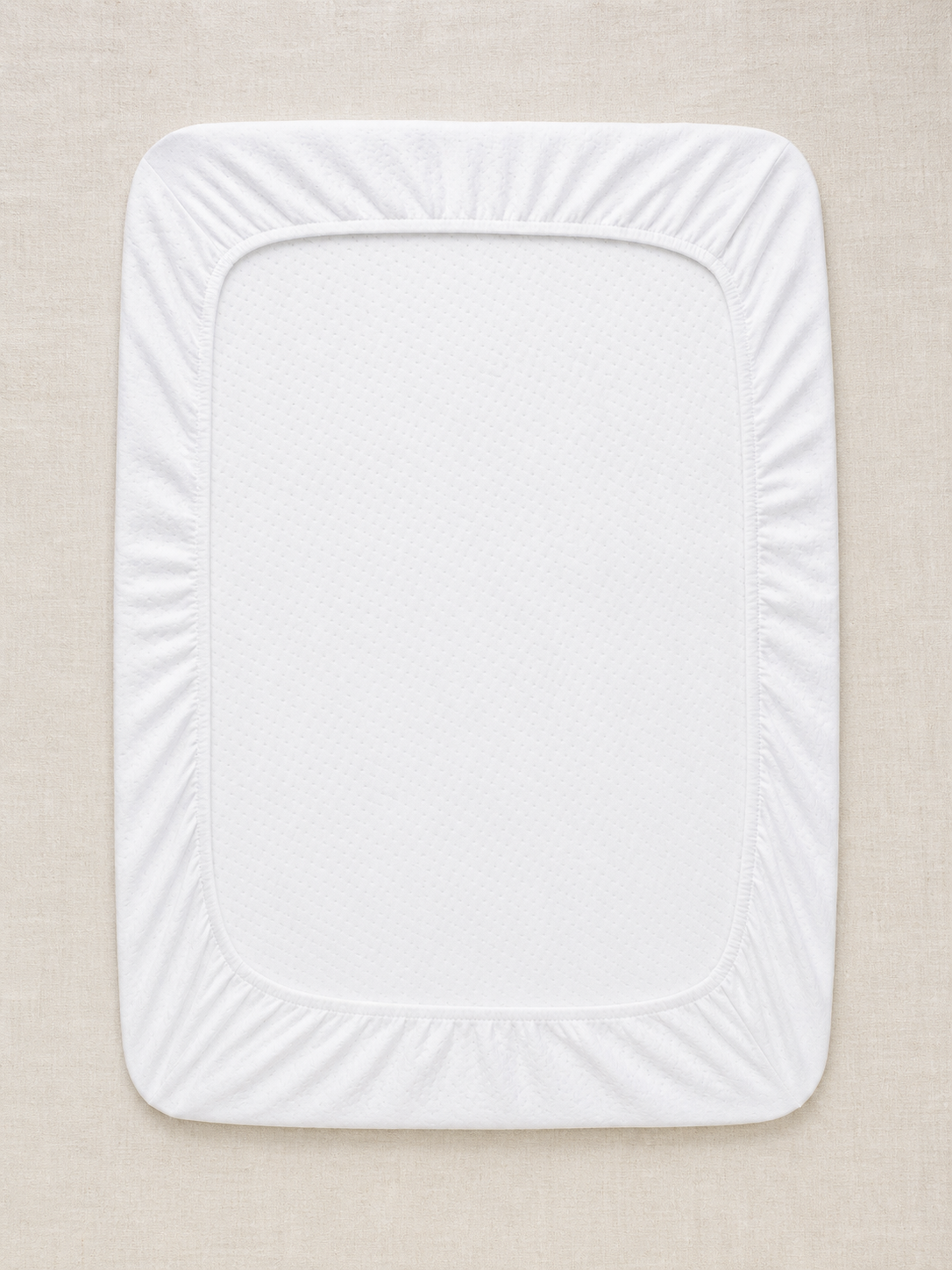 Flat lay of the white waterproof crib mattress protector on oat linen