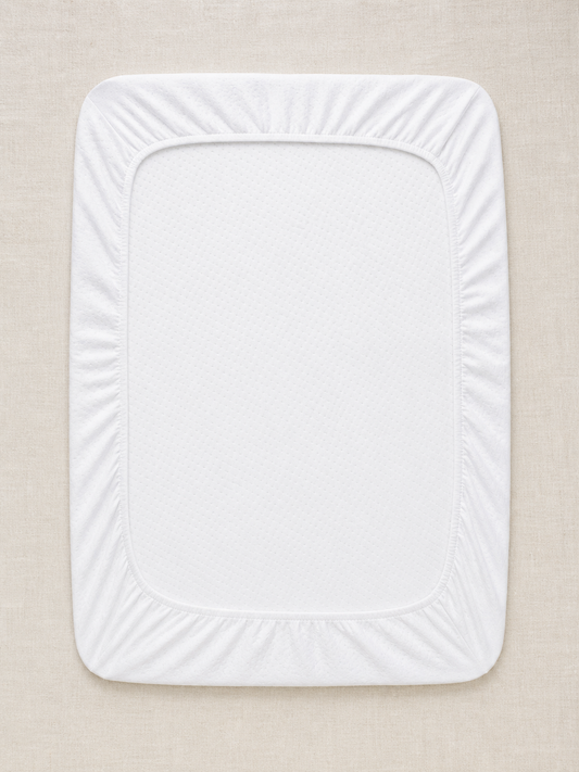 Flat lay of the white waterproof crib mattress protector on oat linen